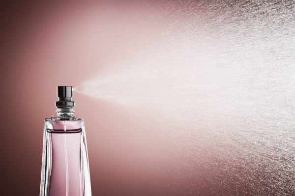 Glass bottle of perfume spraying mist against pink background Glass bottle of pink perfume spraying a fine mist against a pink background